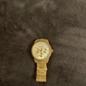 Guldig klocka från Michael Kors - Stilren guldig klocka från Michael Kors med länkarmband och rund urtavla. Klockan har tre mindre urtavlor och detaljerade markeringar. Snygg och klassisk design som sticker ut med sin helguldiga look och robusta länk.