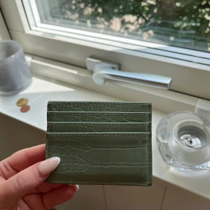 Grön kortplånbok i krokopräglat skinn - Snygg grön kortplånbok med krokodilpräglat mönster. Perfekt för dig som vill ha koll på korten utan att ta plats. Stilren och trendig design med flera kortfack. Passar lätt i fickan eller en mindre väska.
