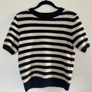 Randig stickad tröja från H&M - Supermjuk stickad tröja från H&M med svartvita ränder. Tröjan har korta ärmar, rund halsringning och en relaxed fit. Perfekt för dig som gillar klassisk stil med en twist. Materialet är stickat och känns riktigt skönt mot huden.