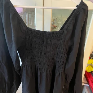 Svart långärmad klänning  - Svart klänning med långa puffiga ärmar. Klänningen har en fyrkantig ringning och är sydd i ett mjukt bomullstyg. Storlek S men passar alla mellan storlek XS-M.