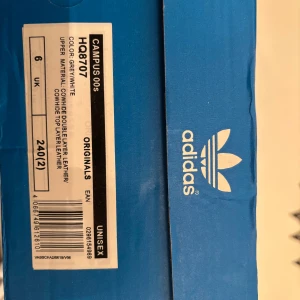 Adidas Campus 00s grå/vita sneakers - Adidas Campus 00s sneakers i grå mocka med vita detaljer och klassiska tre ränder på sidorna. Skorna har vit sula med gummidetalj, rund tå och snörning. Tidlös streetstil med retrovibbar och Adidas logga på plös och häl.