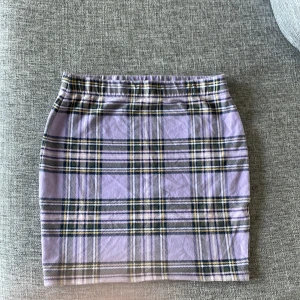 Lila rutig minikjol från Pull&Bear - Superfin lila rutig minikjol från new Yorker  i stretchigt bomullsmaterial. Kjolen har en klassisk rak passform och coolt rutmönster i lila, svart och vitt. Perfekt att styla med en oversized hoodie eller crop top för en trendig look.