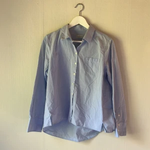 Ljusblå skjorta från Morris - Klassisk ljusblå skjorta från Morris med normal passform. Skjortan har lång ärm, bröstficka och knappar framtill. Tillverkad i mjuk bomull och passar perfekt till jeans eller chinos. Enkel och stilren design som funkar till många olika looks.