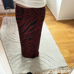 Zebramönstrad långkjol i vinrött - Snygg långkjol med zebramönster i vinrött och svart. Kjolen har en rak passform och resår i midjan för extra komfort. Perfekt för dig som vill sticka ut med ett djurmönster och cool färgkombination.