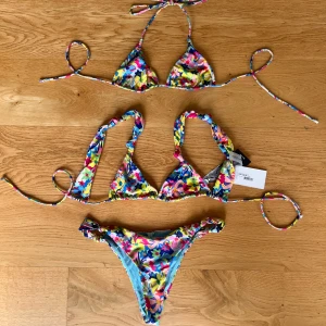 Blommig bikini - Färgglad bikini med blommönster. Säljs som set med två överdelar i olika modeller och en matchande underdel. 