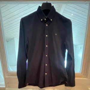 Mörkblå skjorta från Morris  - Snygg mörkblå skjorta från Morris Stockholm i storlek S. Skjortan har klassisk krage med knappar, vita knappar framtill och diskret Morris-logga broderad på bröstet. Tillverkad i bomull med Twofold Yarn för extra komfort och stil.