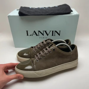 Bruna sneakers från Lanvin i mocka - Snygga bruna sneakers från Lanvin med ovandel i mocka och lackad tå. Skorna har snörning och en vit platt sula som ger en clean look. Perfekta för dig som gillar stilrena och exklusiva sneakers med unika detaljer. (Det förekommer endast dustbag) skorna är i storlek 41 men sitter lite större i storleken. De kan också hämtas i Gbg. Bara höra av er vid frågor eller vid fler bilder🙌