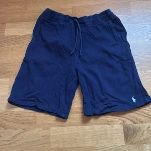 Blå shorts från Polo Ralph Lauren - Mörkblå shorts från Polo Ralph Lauren med snörning i midjan och klassisk logga broderad framtill. Sköna och avslappnade med fickor på sidorna och bak. Perfekta för sommardagar eller chill hemma. Tillverkade i mjuk bomull för extra komfort.