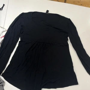 Svart långärmad klänning H&M Mama - En svart, enkel och mjuk långärmad klänning från H&M Mama. Modellen är kort och har en markerad söm under bysten som ger en snygg siluett. Perfekt för dig som vill ha något bekvämt och stilrent.