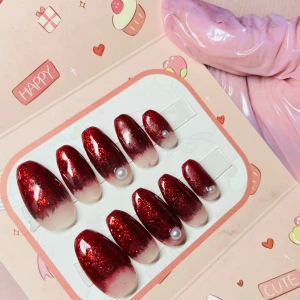 Röda glitter ombre lösnaglar med pärlor - Snygga lösnaglar i mandelform med röd glitter ombre-effekt som tonar ut i nude. Några naglar är dekorerade med små pärlor för extra detalj. Perfekt för dig som vill ha en glam och unik look. Kommer i söt förpackning.