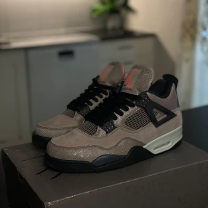 Nike Air Jordan 4 Taupe Haze sneakers - Nike Air Jordan 4 Taupe Haze med sprucken mocka och meshdetaljer. Skorna har svarta snören, svarta och grå detaljer samt orange Jumpman-logga på plös och sula. Snygg kontrast mellan taupe, svart och orange. Perfekta för dig som gillar unika sneakers med streetkänsla.
