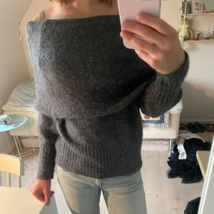 Mörkgrå offshoulder stickad tröja - Mysig mörkgrå stickad tröja med offshoulder-design och ribbade muddar. Perfekt för lager på lager och ger en chill men ändå snygg vibe. Passar till jeans eller kjol för en avslappnad look.