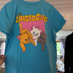 Blå Aristocats t-shirt från Disney - Snygg blå t-shirt från Disney med färgglatt tryck av Aristocats-kattungarna på framsidan. T-shirten har korta ärmar, rund hals och är gjord i mjuk bomull. Perfekt för dig som älskar retro och tecknade filmer!
