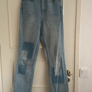 Ljusblå raka jeans med patchar - Säljer ett par ljusblå jeans med raka ben och coola patchade detaljer på framsidan. Jeansen har hög midja, klassiska bakfickor och är tillverkade i denim. Perfekta för dig som gillar en unik och avslappnad stil.