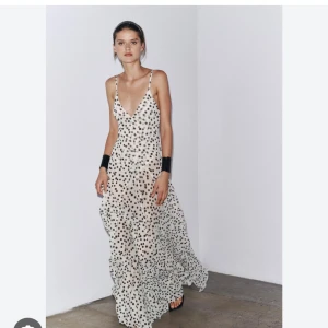 Söker XS eller S  - Söker  en lång, flowy klänning i vitt med svarta prickar och smala axelband. Klänningen har v-ringning och är ärmlös, perfekt för sommarens alla tillfällen. Den har en luftig och lätt känsla som ger en cool vibe.