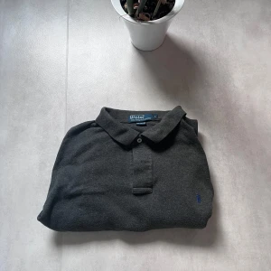 Mörkgrå långärmad pikétröja Polo Ralph Lauren - Polo Ralph Lauren långärmad piké – Storlek L 🖤 Stilren mörkgrå färg med blå broderad logga ✅ Väldigt bra skick – inga defekter 🧼 Nyttvättad och redo att användas 👕 Passar perfekt till höst och lager-på-lager-look  💸 Säljes billigt – först till kvarn! 📩 Skriv DM vid minsta fundering 🙌 