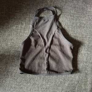 Svart ribbad croppad linnetopp XS - Säljer en svart croppad linnetopp med ribbad struktur och smala axelband som korsas i ryggen. Toppen har hög halsringning och är tillverkad i stretchigt material som sitter snyggt på kroppen. Perfekt för en trendig och sportig look.