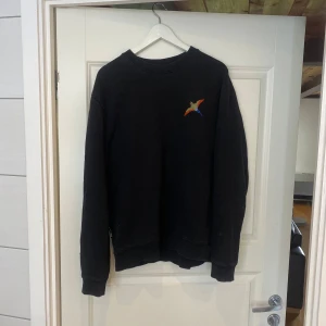 Svart sweatshirt från Axel Arigato - Svart sweatshirt från Axel Arigato med broderad färgglad fågel på bröstet. Tröjan har rund hals, ribbade muddar och en relaxed passform. Perfekt för dig som gillar stilrena plagg med en twist.