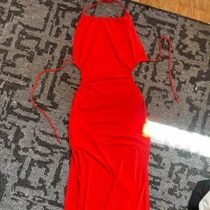 Röd långklänning med snörning - Snygg röd långklänning från Bershka med halterneck och smala knytband i nacken och midjan. Klänningen har en figurnära passform, slits på sidan och är ärmlös. Perfekt för dig som vill sticka ut med en färgstark look.