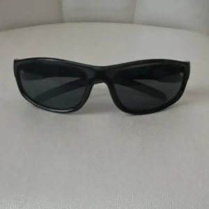 Svarta sportiga solglasögon - Snygga svarta solglasögon med sportig design och breda bågar. Perfekta för dig som gillar en clean och stilren look.