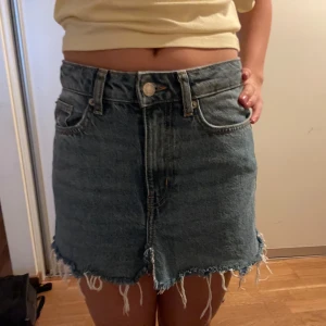 Jeanskjol med fransig kant - Säljer en blå jeanskjol med rå, fransig nederkant och klassiska fickor fram och bak.