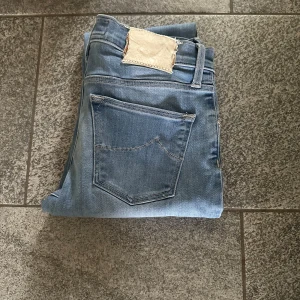 Jacob Cohën Jeans - Säljer ett par ljusblå jeans från Jacob Cohën med klassisk femficksdesign och broderad J på myntfickan. Jeansen har raka ben och är tillverkade i mjukt denimtyg som ger en avslappnad vibe. Perfekta för dig som gillar stilrena och tidlösa jeans. 