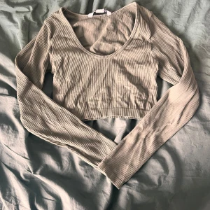 Grön ribbad croppad långärmad topp - Trendig croppad topp i grön med ribbad struktur och långa ärmar. Djup rundad urringning ger en snygg siluett och passar perfekt till höga jeans eller kjol. Mjuk och stretchig för en bekväm känsla hela dagen.