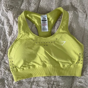 Gul sporttopp från Gymshark  - Snygg gul sporttopp från Gymshark i storlek M. Toppen har brottarrygg, ribbade detaljer samt små hål som detaljer. Tillverkad i stretchigt material som sitter super skönt. 