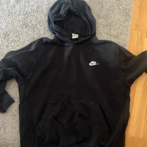 Svart Nike hoodie med huva - Svart hoodie från Nike med klassisk logga på bröstet. Tröjan har huva, känguruficka och långa ärmar. Perfekt för chill dagar eller när du vill ha en enkel och stilren look.