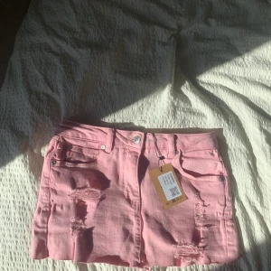 Rosa jeanskjol med slitningar - Hej, säljer en super söt rosa jeans kjol med hål i som är lågmidjad, den är helt ny, storlek 36, skriv om ni undrar något❤️