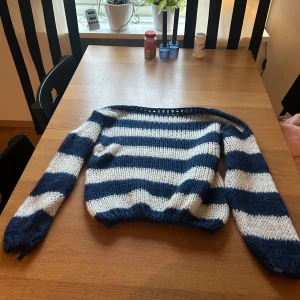 Randig stickad tröja i blått och vitt - Säljer en stickad tröja med breda blå och vita ränder. Tröjan har lång ärm och en klassisk, lite loose passform. Perfekt för dig som gillar en chill och mysig stil. Ribbstickad vid ärmslut och nederkant.