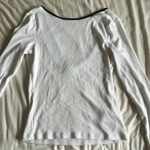 Vit ribbad topp från Gina Tricot - Säljer en vit långärmad ribbad topp från Gina Tricot i storlek M. Toppen har en djup, rundad urringning i ryggen med svart kant och är tillverkad i ett stretchigt material som sitter snyggt på kroppen. Perfekt att styla med jeans eller kjol.