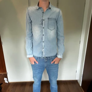 Ljusblå jeansskjorta med knappar - Snygg ljusblå jeansskjorta med klassisk krage och bröstficka. Skjortan har knappar hela vägen och lång ärm, perfekt för en avslappnad men stilren look. Passar dig som gillar denim och vill ha något enkelt men ändå trendigt.