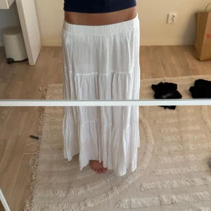 Vit långkjol från Stradivarius - Superfin vit långkjol från Stradivarius med resår i midjan och snyggt fall. Kjolen är i tunn, lätt bomull och har flera volanger som ger en luftig och chill vibe. Perfekt för varma dagar och enkel att styla med crop tops eller linnen.