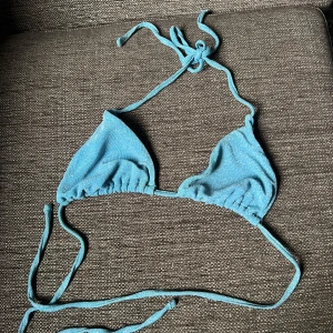 Blå glittrig trekantsbikini - Supersnygg blå trekantsbikini med glittrigt tyg och knytband i nacken och ryggen. Klassisk modell med tunna band och skimrande yta som verkligen poppar i solen. Perfekt för stranden eller poolen i sommar!