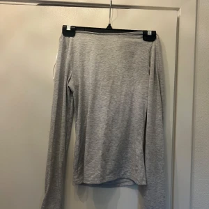 Ljusgrå långärmad topp med öppen rygg - Supersnygg ljusgrå långärmad topp i mjuk bomullsblandning. Toppen har en unik öppen rygg med twistad detalj upptill som ger en cool och trendig look. Perfekt till jeans för en avslappnad men ändå stylish outfit.