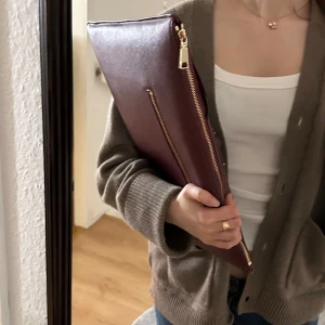 Vinrött datorfodral  - Stilren vinrött datorfodral från ideal of sweden i slätt skinn. Datorfodralet har guldfärgade detaljer, en smal dragkedja på baksidan och en större dragkedja upptill. Fodralet har en liten skada vid dragkedjan, fråga gärna om ni undrar något! ❣️