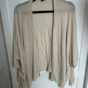 Beige kofta från Gina Tricot XS/S - Luftig och tunn beige kofta från Gina Tricot i storlek XS/S. Modellen är öppen framtill med avslappnad passform och har ett snyggt fall. Perfekt att slänga över en topp under vår eller sommarkvällar.