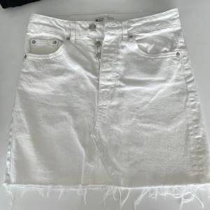 Vit jeanskjol från g perfect jeans - Vit kort jeanskjol med rå kant nertill och klassiska femficksdetaljer. Kjolen har knappar framtill och bälteshällor i midjan. Perfekt för en fräsch och avslappnad look under varma dagar.