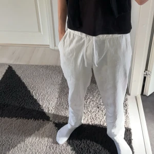 Vita linnebyxor - Säljer ett par fräscha vita linnebyxor med dragsko i midjan. Byxorna har avslappnad passform, raka ben och sidfickor. Perfekta för varma dagar när du vill ha något svalt och stilrent. Passar både chill och cityhäng.
