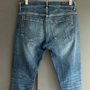 Dondup George W33 - Klassiska blå Dondup jeans med raka ben och slitningar på knäna. Byxorna har knappar i gylfen, fem fickor och tydliga slitdetaljer framtill. Perfekta för en avslappnad stil. Bra skick. Storlek W33 passar folk runt 180. Mitt pris 400kr nypris runt 3000kr. Kontakta mig om du har frågor✅