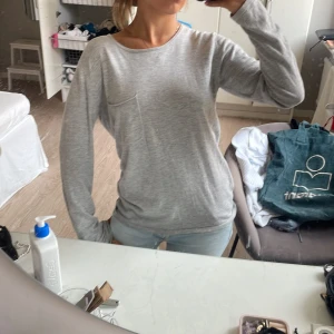 Ljusgrå långärmad tröja - Enkel och stilren ljusgrå långärmad tröja med rund halsringning och liten bröstficka. Tröjan har en avslappnad passform och är perfekt för en chill vardagslook. Tillverkad i mjukt material som känns skönt mot huden.