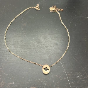 Guldigt halsband med rund berlock - Snyggt halsband i guldton med tunn kedja och en rund berlock med utskuret kors och liten glittrig detalj. Perfekt accessoar för att lyfta din outfit med en stilren touch.