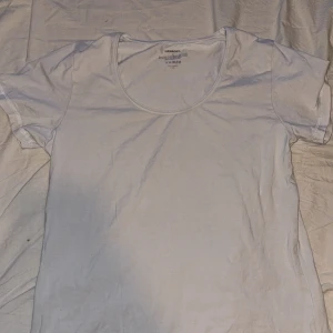 Vit basic t-shirt från Newbody XL - Enkel och stilren vit t-shirt från Newbody i storlek XL. T-shirten har rund halsringning och korta ärmar. Tillverkad i mjuk bomull med lite stretch för extra komfort. Perfekt till jeans eller shorts för en clean look.