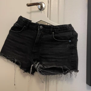 Svarta jeansshorts med fransig kant - Svarta jeansshorts från Gina Tricot med rå, fransig kant och klassisk femficksmodell. Shortsen har låg midja och en cool, sliten look som passar perfekt till sommaren. Materialet är denim och de har en normal passform.