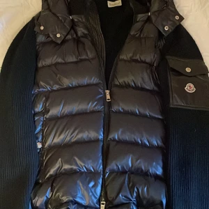 Svart moncler cardigan - Snygg svart moncler cardigan! Som har glansigt dunmaterial med luva! Jackan har en dragkedja upp till huvudet/ halsen. Jackan är i bra skick och 100% äkta men kommer med inga kvitton. Men om man vill ha mer äktighets bevis är det bara att kontakta mig!😄