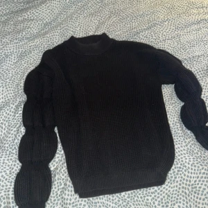 Svart stickad tröja från Pieces - Svart stickad tröja från Pieces i storlek XS. Tröjan har en högre rund hals och unika puffade ärmar med flera sektioner som ger en cool och trendig look. Perfekt för dig som vill ha något extra i garderoben.