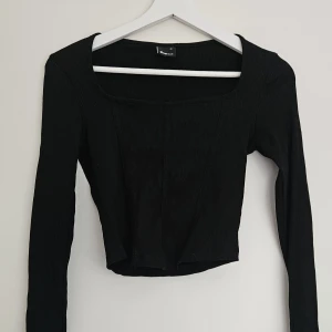 Svart croppad långärmad topp - Svart croppad topp från Gina Tricot med lång ärm och fyrkantig urringning. Toppen är ribbad med en figurnära passform. Oanvänd. Storlek M