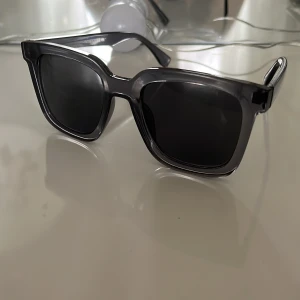 Grå fyrkantiga solglasögon - Stilrena solglasögon med grå, fyrkantig båge i plast och mörka linser. Perfekt accessoar för att lyfta din look och skydda ögonen mot solen. Klassisk design som funkar till det mesta.