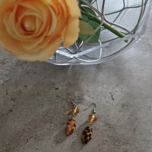 Leopardmönstrade örhängen med pärlor - Coola örhängen med leopardmönstrade droppformade pärlor och facetterade bärnstensfärgade pärlor upptill. Hängande modell med metallkrok. Perfekta för dig som vill sticka ut med ett djurmönster och varma färger.